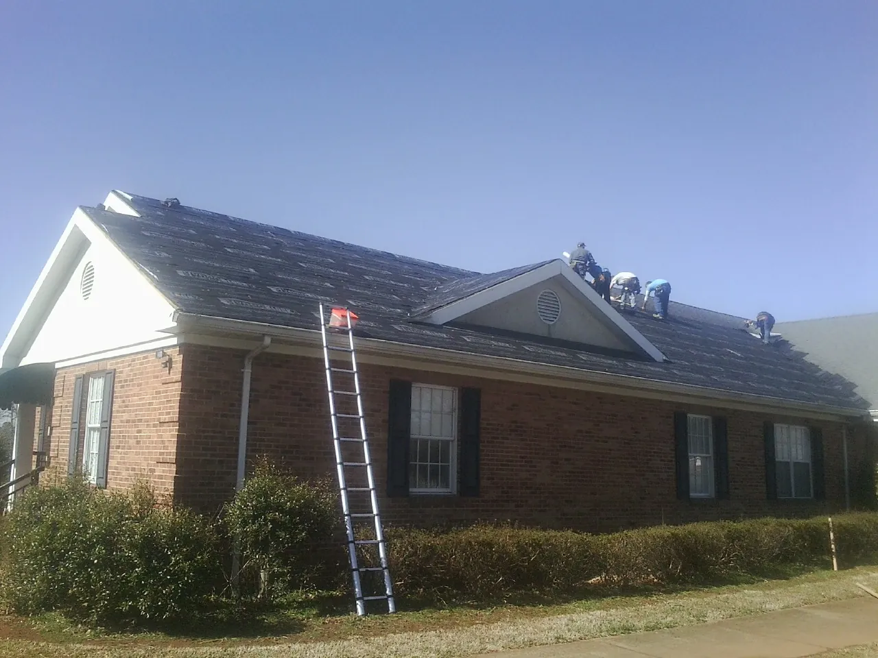 Crew tearing shingles off a brick ranch roof with a ladder set — Emergency Roof Repair work by our crew in South Hackensack