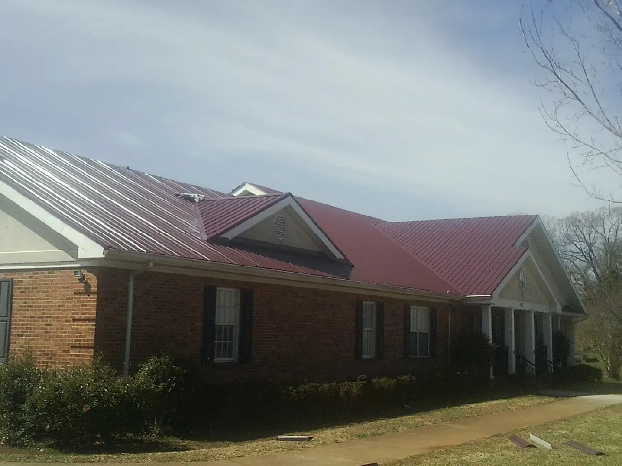 Red metal roof with gabled entries on a long brick building, from a Hail Damage Roof Repair job in South Hackensack