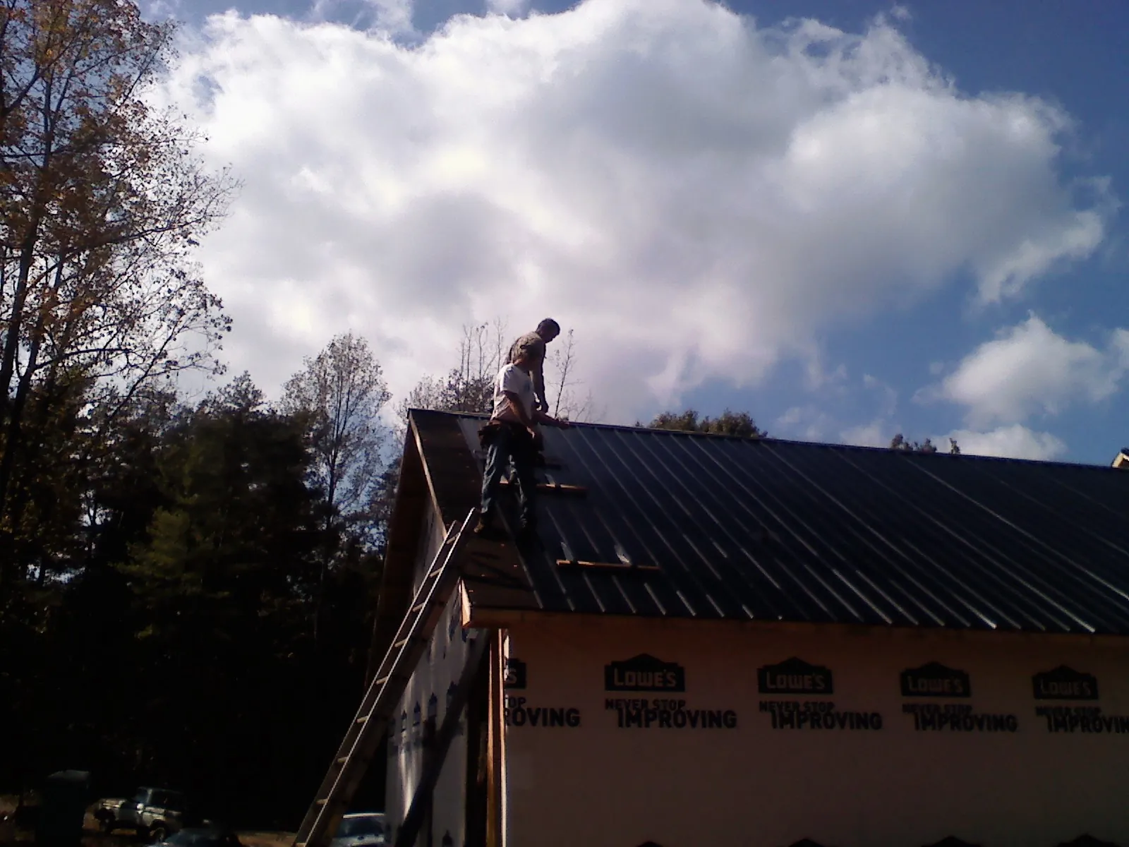 Roofer fastening dark metal panels high against a cloudy sky, from a Roof Inspection job in South Hackensack